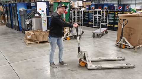 worker maneuvering a manual pallet jack in a warehouse, face visible