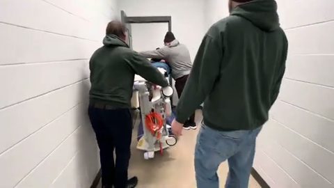 movers angling a hospital bed through a narrow doorway
