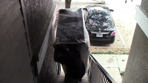 mover carrying a shrink-wrapped sofa up apartment exterior stairs