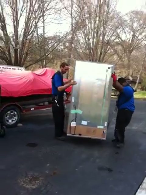 two movers carrying a stainless refrigerator across a driveway, face visible