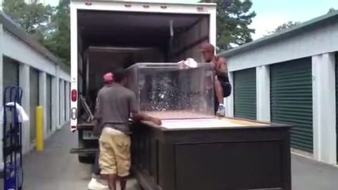 movers lowering a large glass aquarium onto a cabinet base, face visible