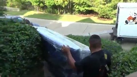 two movers carrying a wrapped couch toward a moving truck at the curb