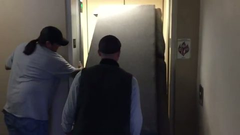 two-man crew loading a wrapped mattress into an elevator