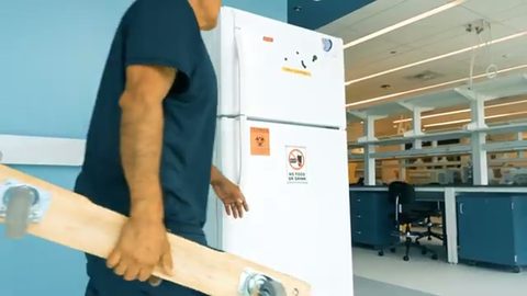 mover wheeling a lab freezer on a furniture dolly through a lab