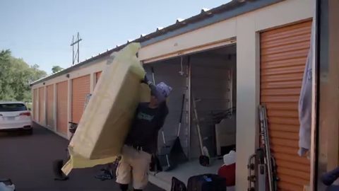 mover carrying a wrapped mattress into a storage unit